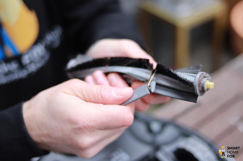 Hair is removed from the brush of the Ecovacs Deebot X1 OMNI using a cleaning tool.